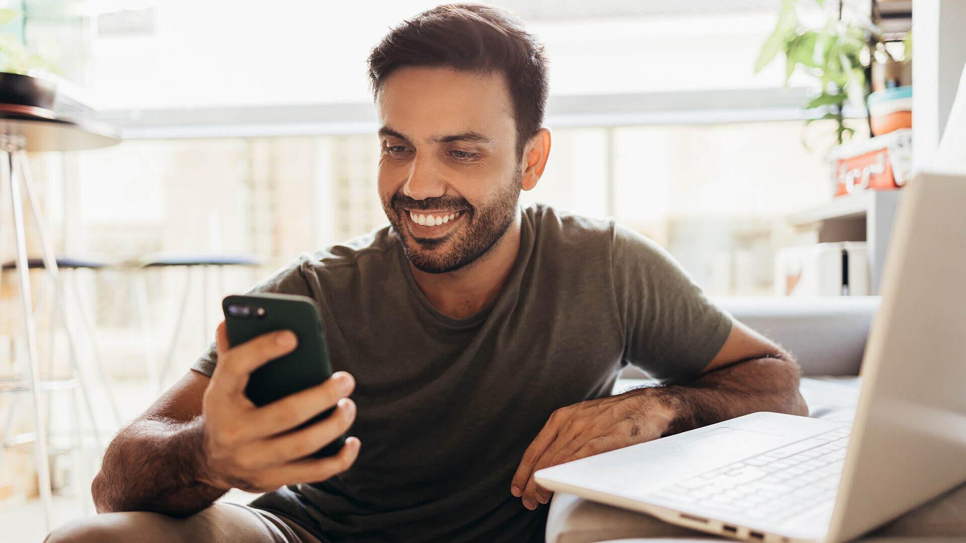 homem olhando para o smartphone e laptop