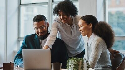 Duas pessoas sentadas e uma em pé apontando para o notebook