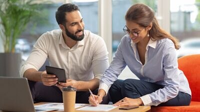 Um homem e uma mulher no sofá com documentos e um notebook sobre a mesa