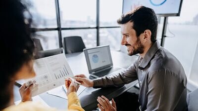 Um homem em uma sala de reunião com uma mulher que está apresentando gráficos em um papel