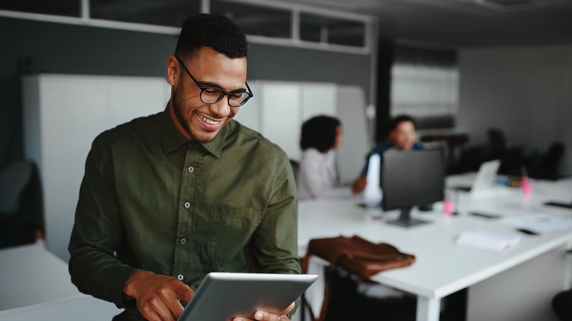 Homem feliz usando um tablet enquanto sues colegas trabalham ao fundo