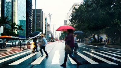 Pessoas com guarda-chuva atravessando a avenida paulista na faixa de pedestre