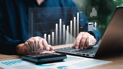Mãos digitando no computador e calculadora com gráficos